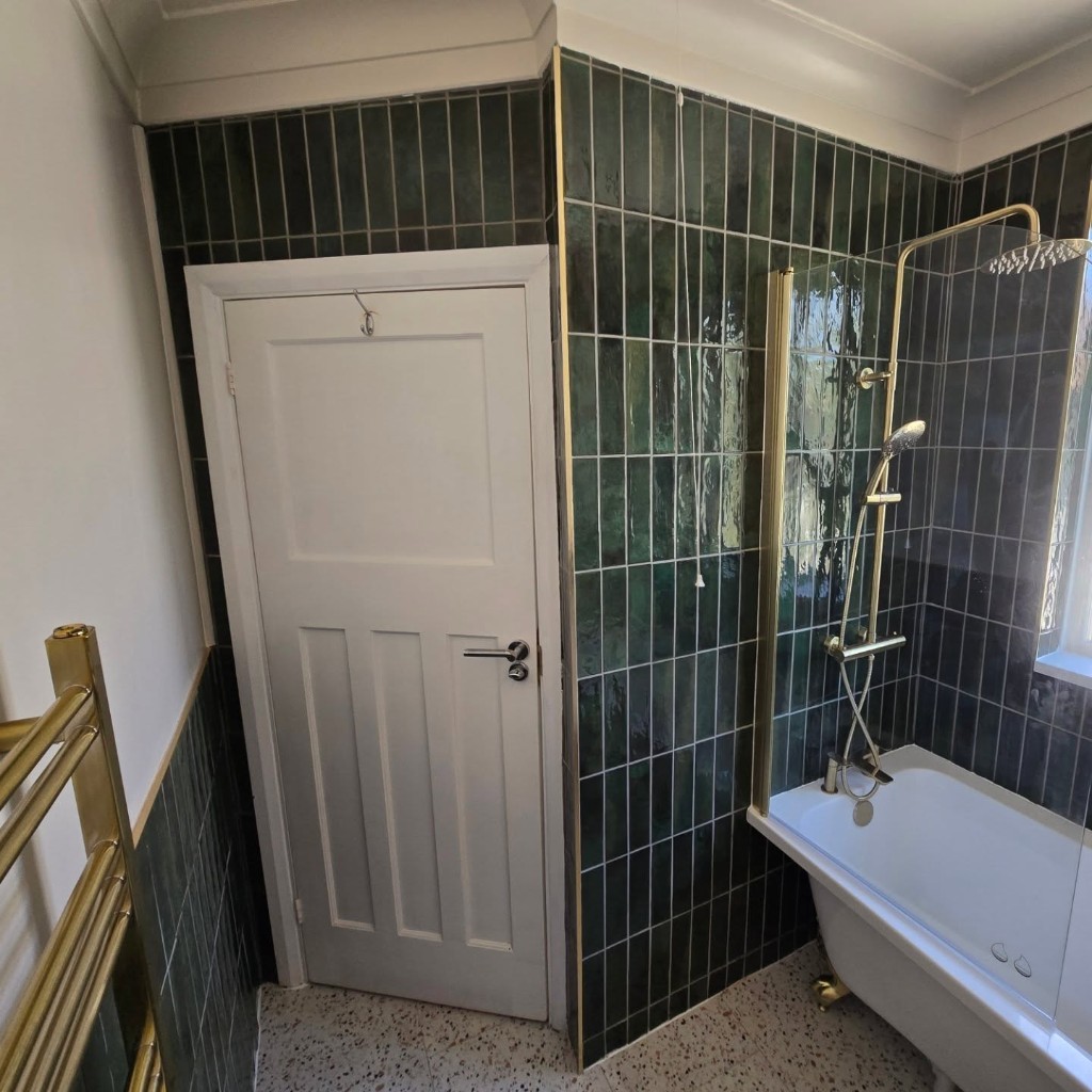 White door and deep green tiling in the redesigned bathroom