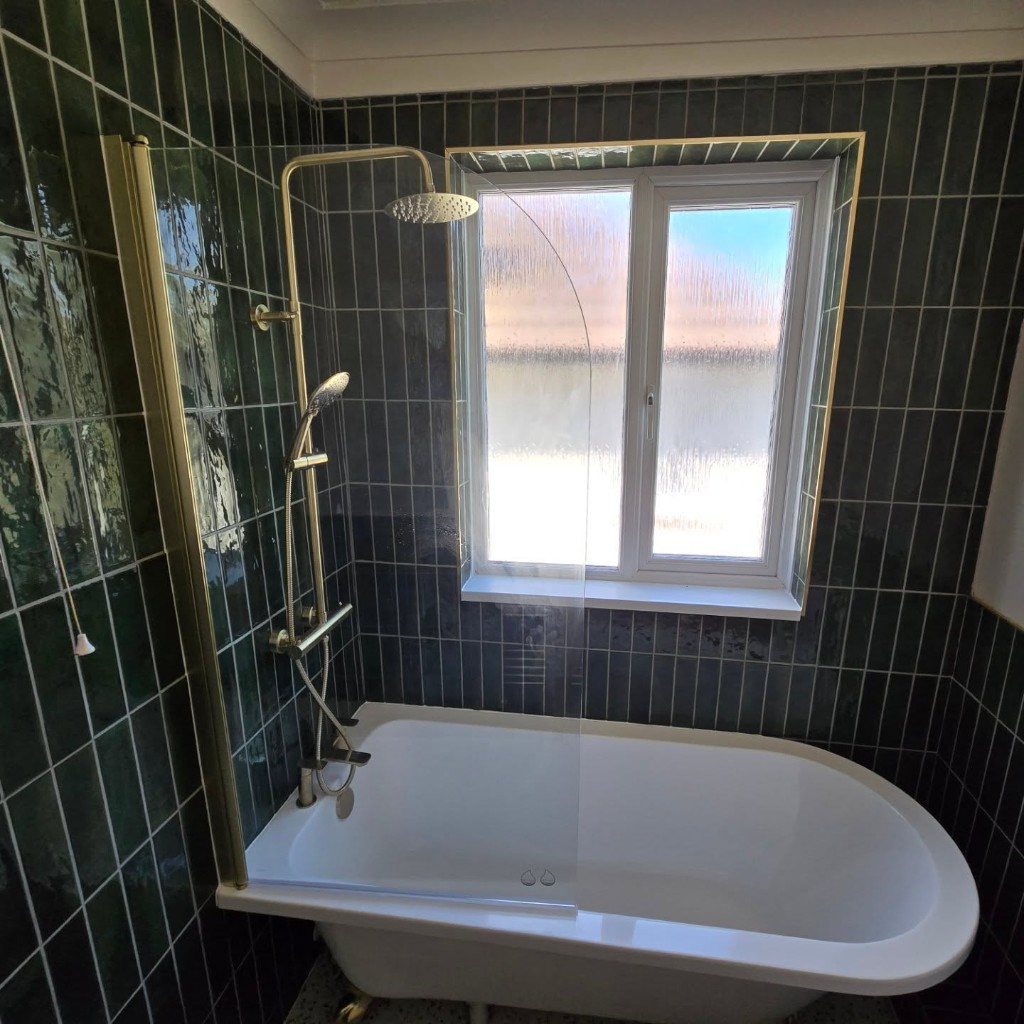 Brushed gold shower and bath screen beside the frosted window