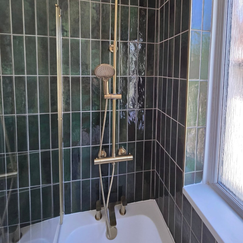 Brushed gold shower valve and handset on the green tiled wall