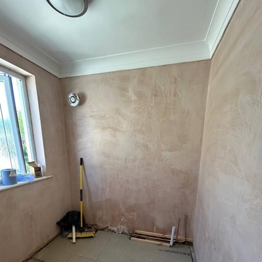 The bathroom stripped back to bare plaster, with the pipework exposed