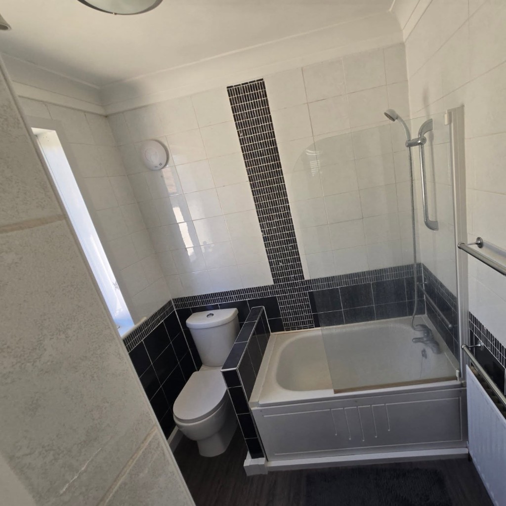 The original bathroom, with white tiles, a black mosaic strip and a panelled bath