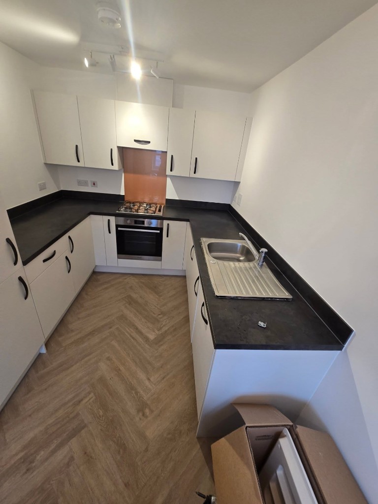 The kitchen before the worktop was replaced, with a dark worktop, stainless sink and splashback behind the hob
